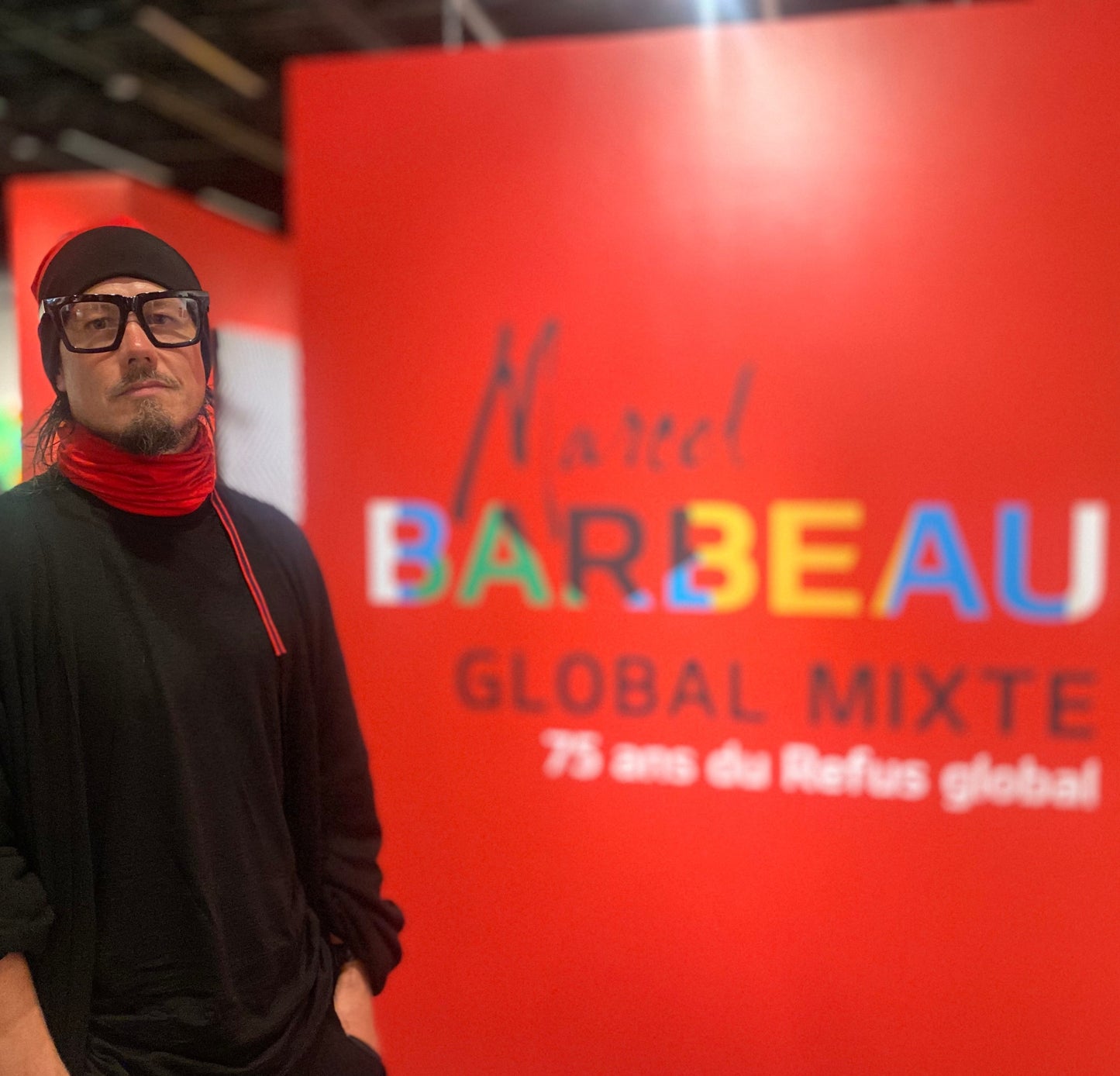 Jonathan Brunelle pose devant l'accueil de l'exposition Marcel Barbeau : Global mixte au Musée des beaux-arts de Mont-Saint-Hilaire pour célébrer les 75 ans de la parution du Refus global.