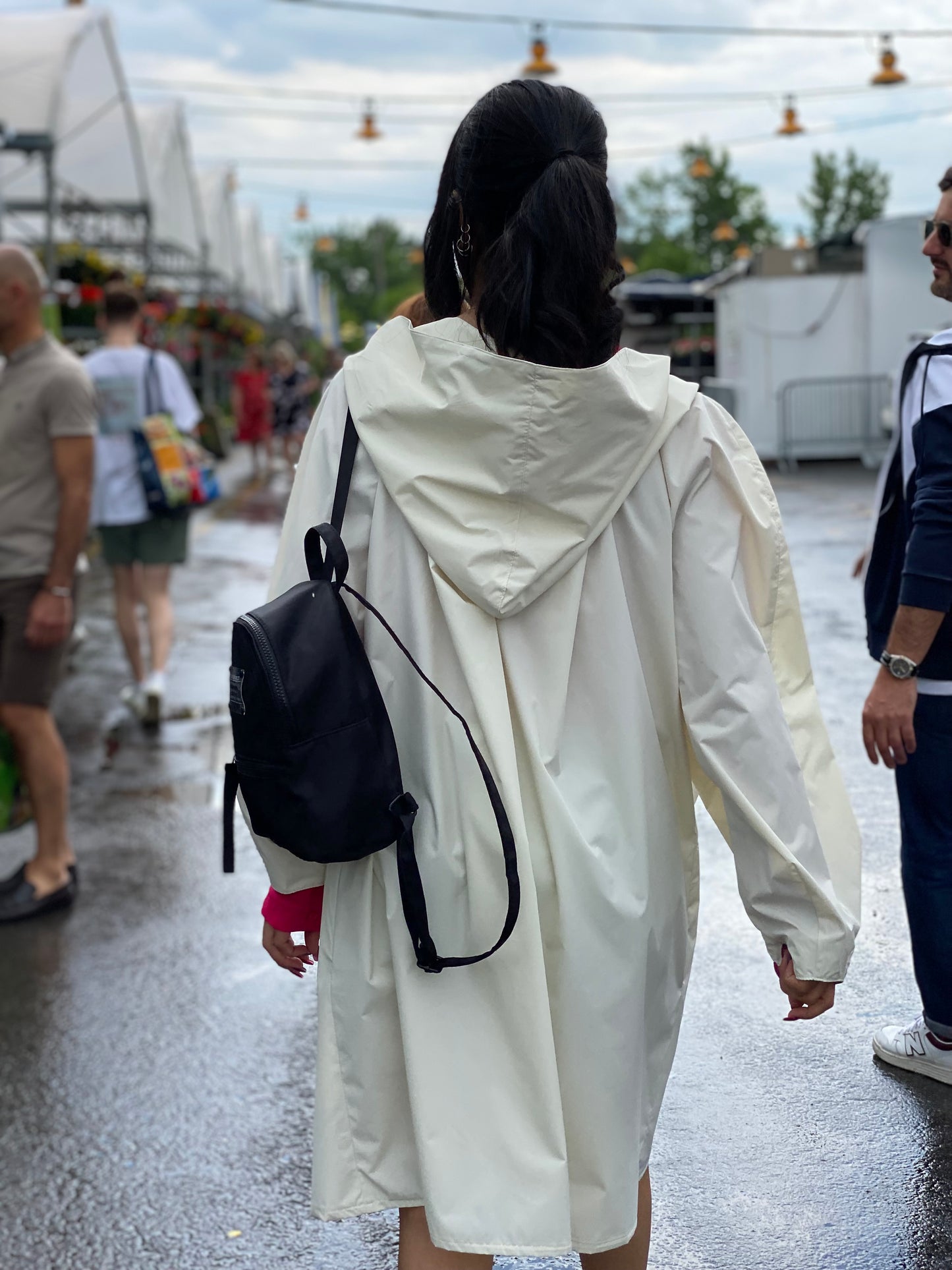 Back view when Sanaz wears an ELZI Waterproof White Raincoat in front of the atwater market. Vue de dos; Sanaz porte un imperméable blanc ELZI devant le marché atwater.